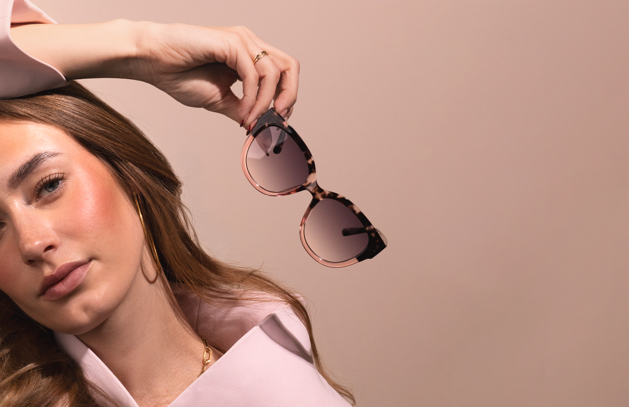 Woman holding a pair of oozoo sunglasses against a beige background